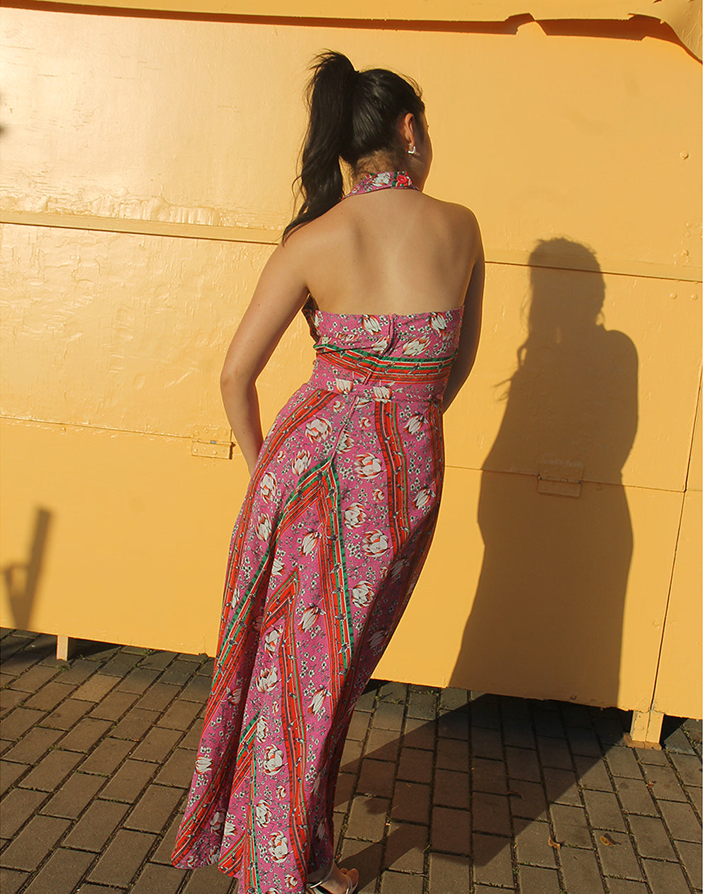 woman wearing 70s pink sleeveless maxi dress against a yellow wall