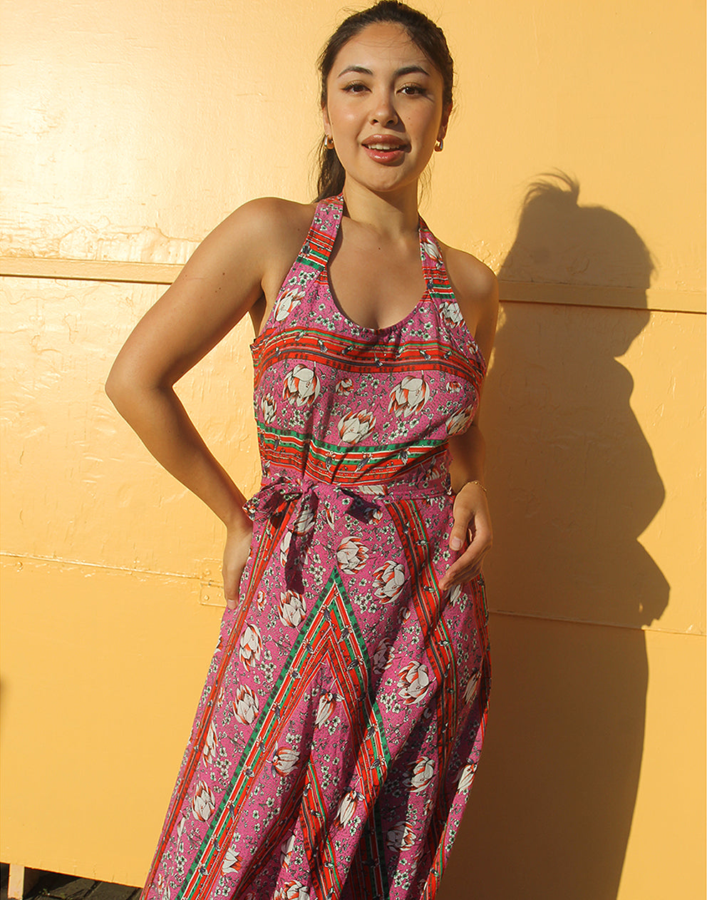 woman wearing 70s pink sleeveless maxi dress against a yellow wall