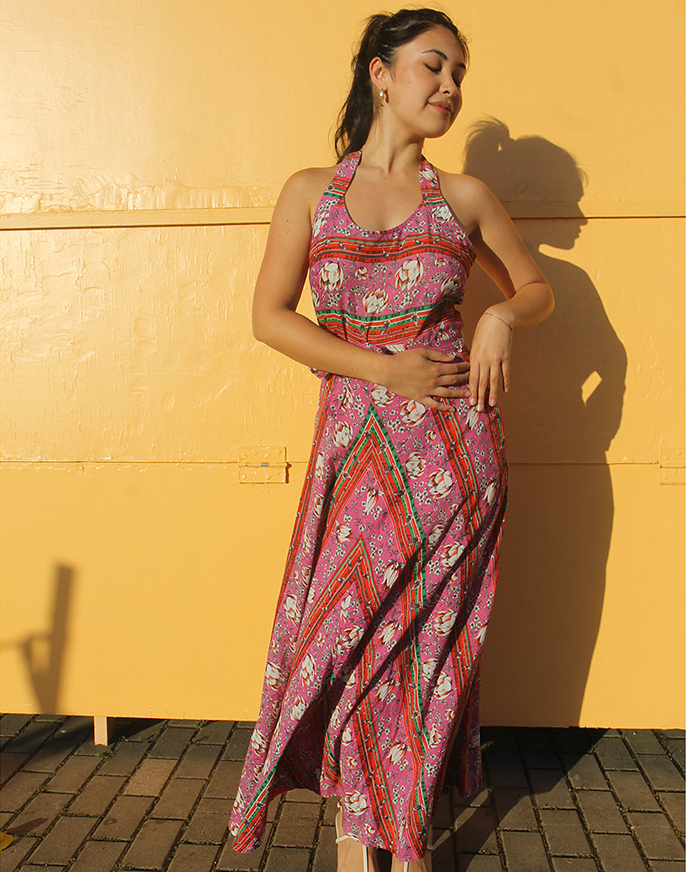 woman wearing 70s pink sleeveless maxi dress against a yellow wall