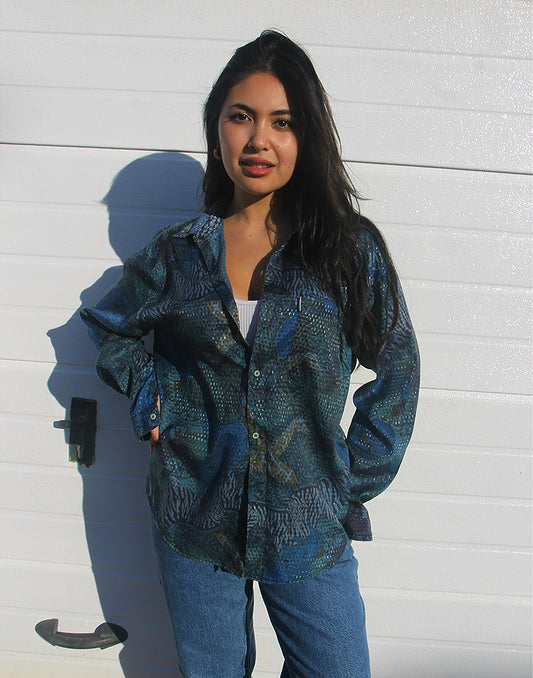 Woman wearing a blue vintage long sleeve shirt standing against a white wall.