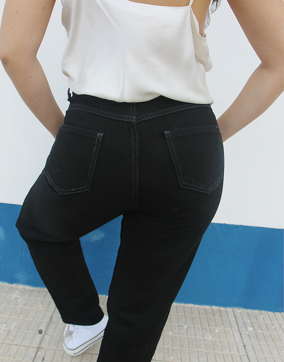 woman wearing black straight leg high rise jeans against a white wall